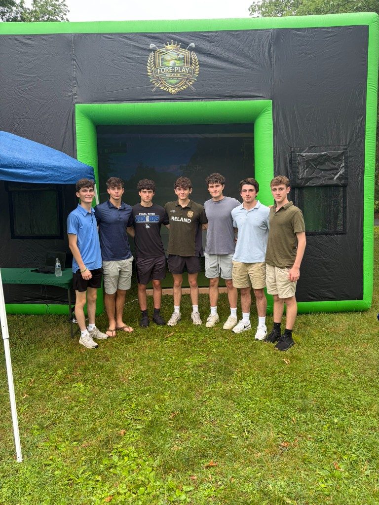 Group of friends posing in front of the Fore-Play Golf simulator at a Pearl River grad party.