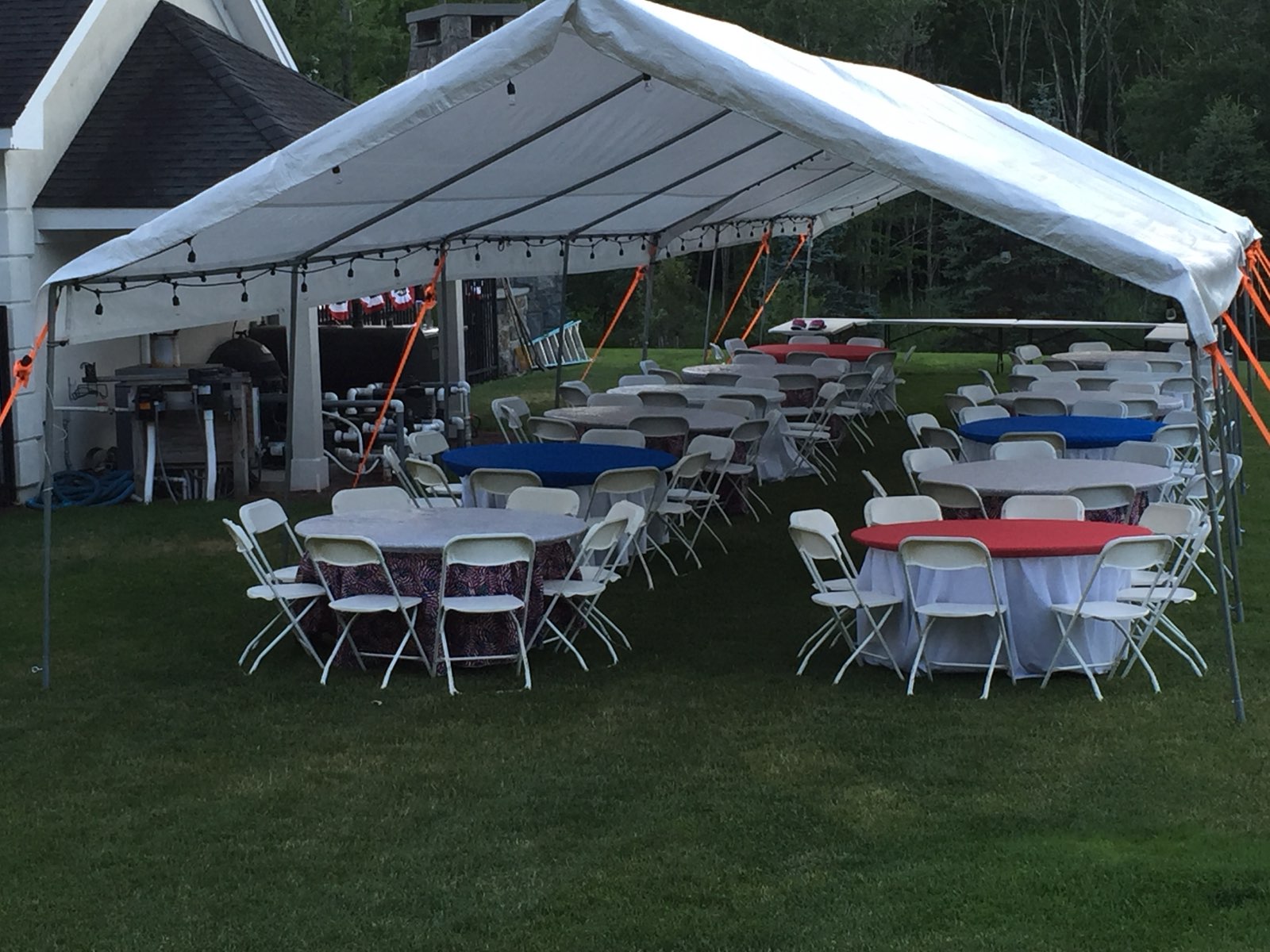 White party tent with round tables, chairs, and string lights on a lawn.